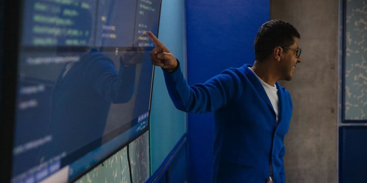 Mann in blauer Jacke zeigt während einer Schulung auf einen Computerbildschirm.